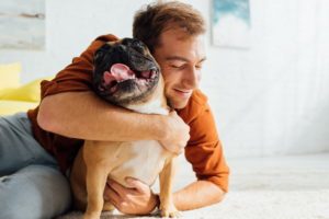 smiling-man-hugging-funny-french-bulldog-on-floor-in-living-room